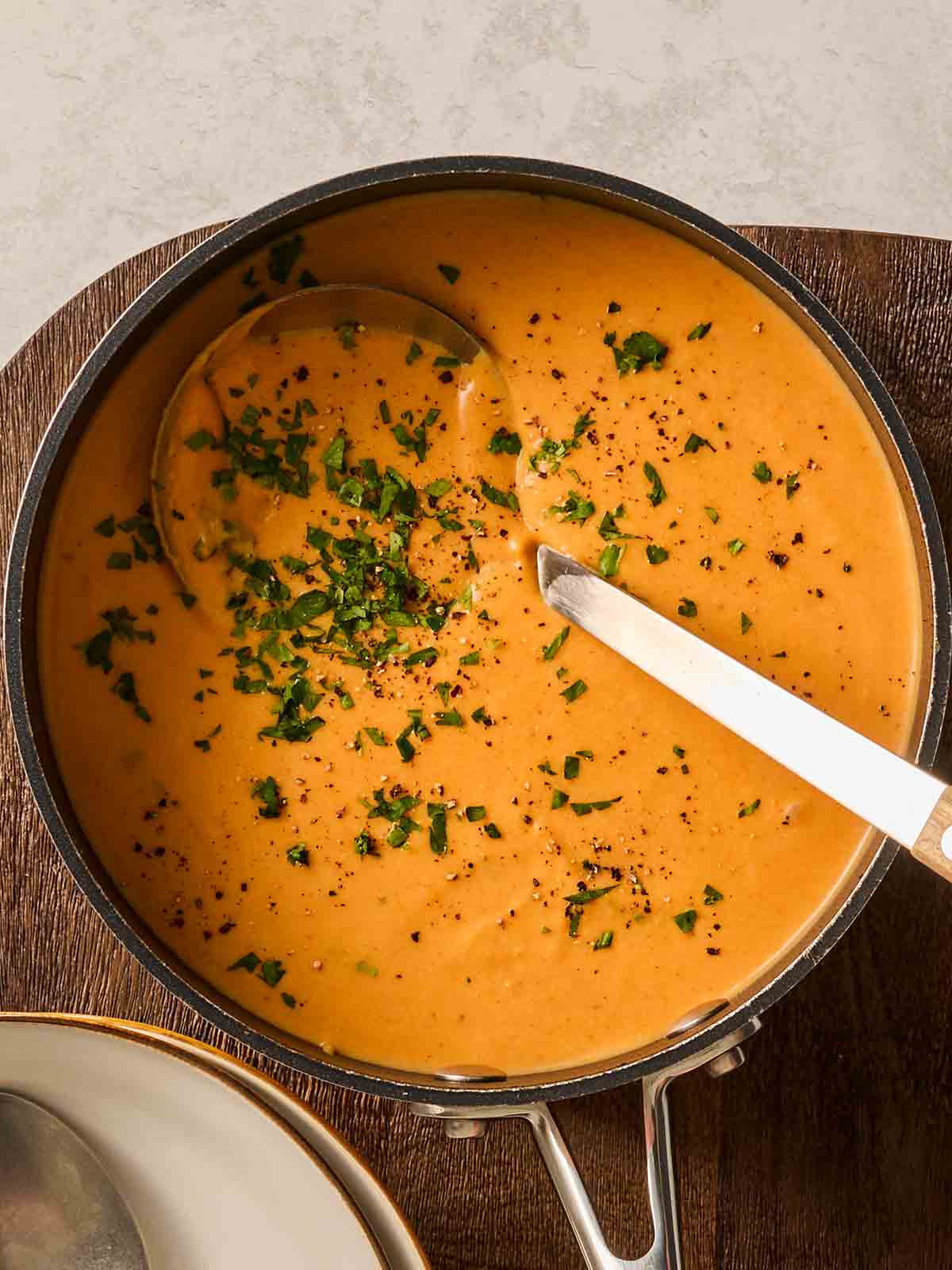 A large pan of sweet potato soup with a ladle inside, ready to serve up and garnished with coriander.